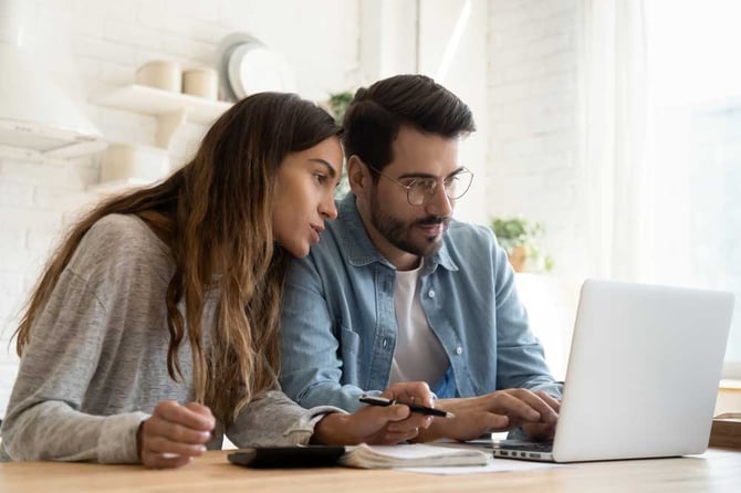 Uma mulher de camisa cinza e um homem de camisa azul olhando para a tela de um notebook realizando a devolução de pagamento