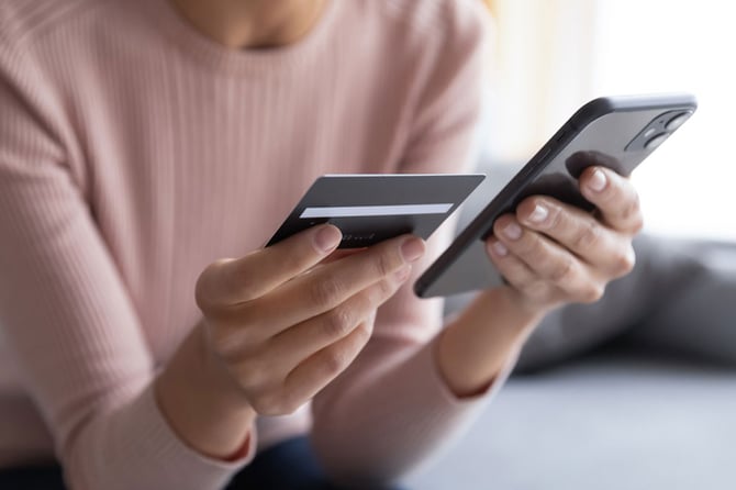 Uma mulher segurando um celular e um cartão em cada mão.