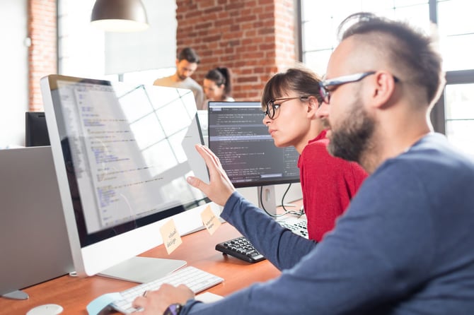 Homem olhando para o computador enquanto faz uma explicação para uma mulher sobre os canais para developers do Mercado Pago anais para developers do Mercado Pago