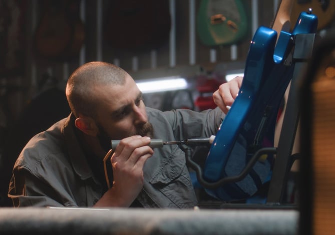 Profissional da música trabalha como luthier soldando fios de guitarra elétrica em sua oficina, representando o empreendedorismo com apoio do Mercado Pago para receber e organizar suas vendas