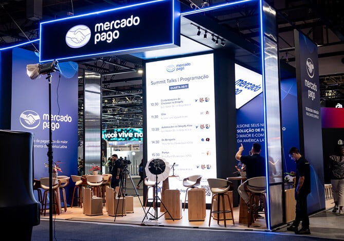 Imagem do estande do Mercado Pago no RD Summit 24 mostrando a programação do SummitTalks, com diversas palestras