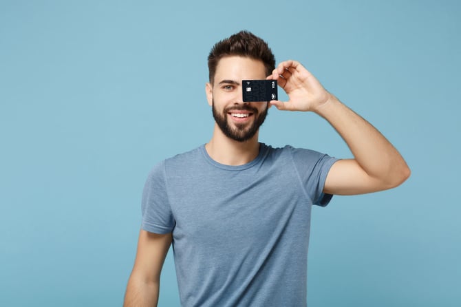 Homem de camiseta azul segurando um cartão Mercado Pago em frente a um dos olhos