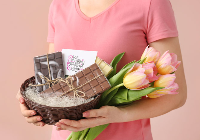 Mercado Pago: imagem dos braços de uma pessoa segurando uma cesta com barras de chocolates como um exemplo de cestas personalizadas e um buquê de tulipas.