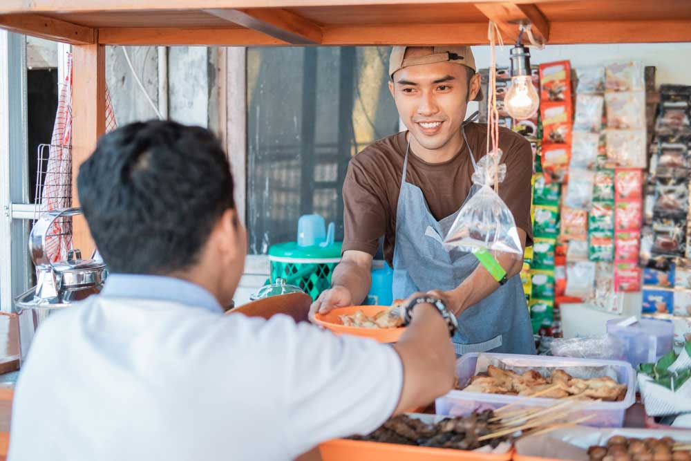 Um vendedor asiático em uma barraca de alimentos atendendo seus clientes.