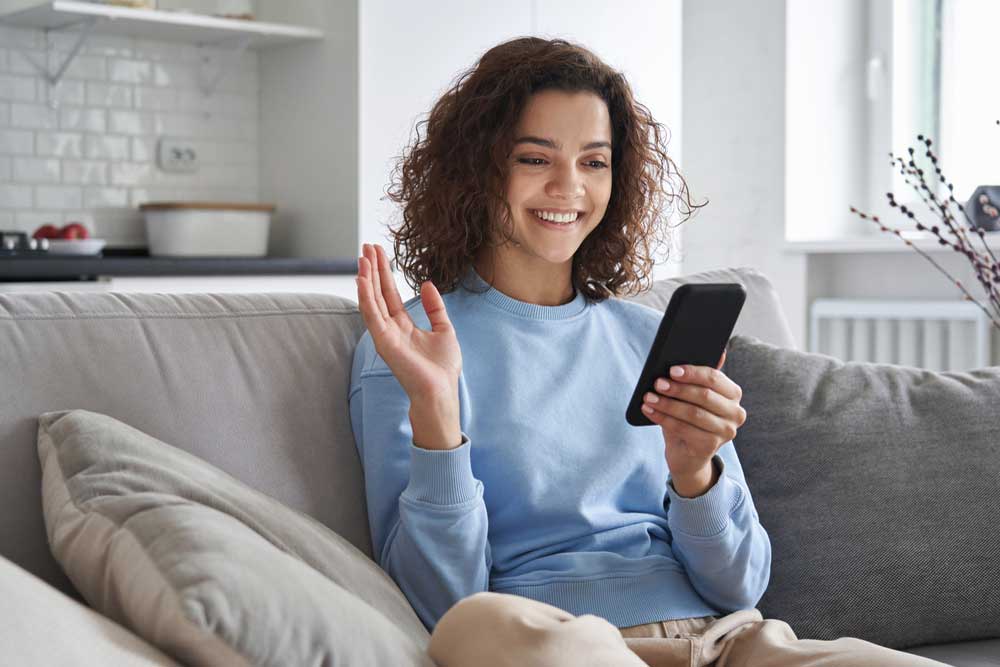 Uma mulher sentada em um sofá segurando um celular na mão esquerda e com a mão direita levantada