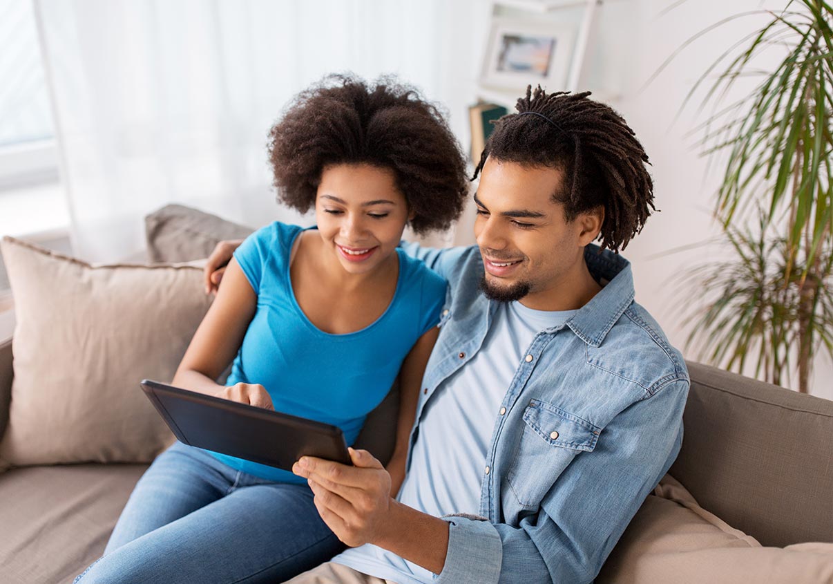 Casal sentado no sofá enquanto mexem no tablet