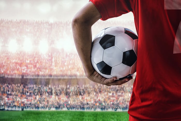 Jogador vestindo camisa vermelha 7, segurando a bola de futebol dentro do estádio lotado de torcedores, sugerindo que o Mercado Pago é o patrocinador da transmissão do Campeonato de futebol Brasileirão 2025.
