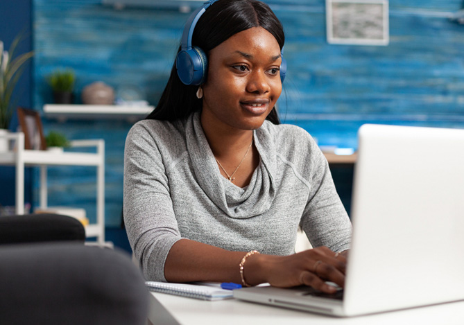 Mulher preta/negra com fone de ouvido usando o laptop para se inscrever no curso de Empreendedorismo Digital do Mercado Pago e Mercado Livre