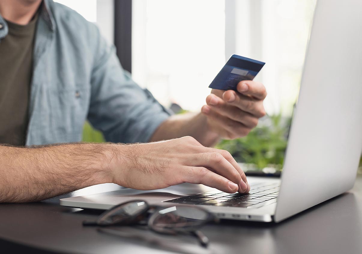 Pessoa segurando cartão de crédito enquanto digita informações no laptop