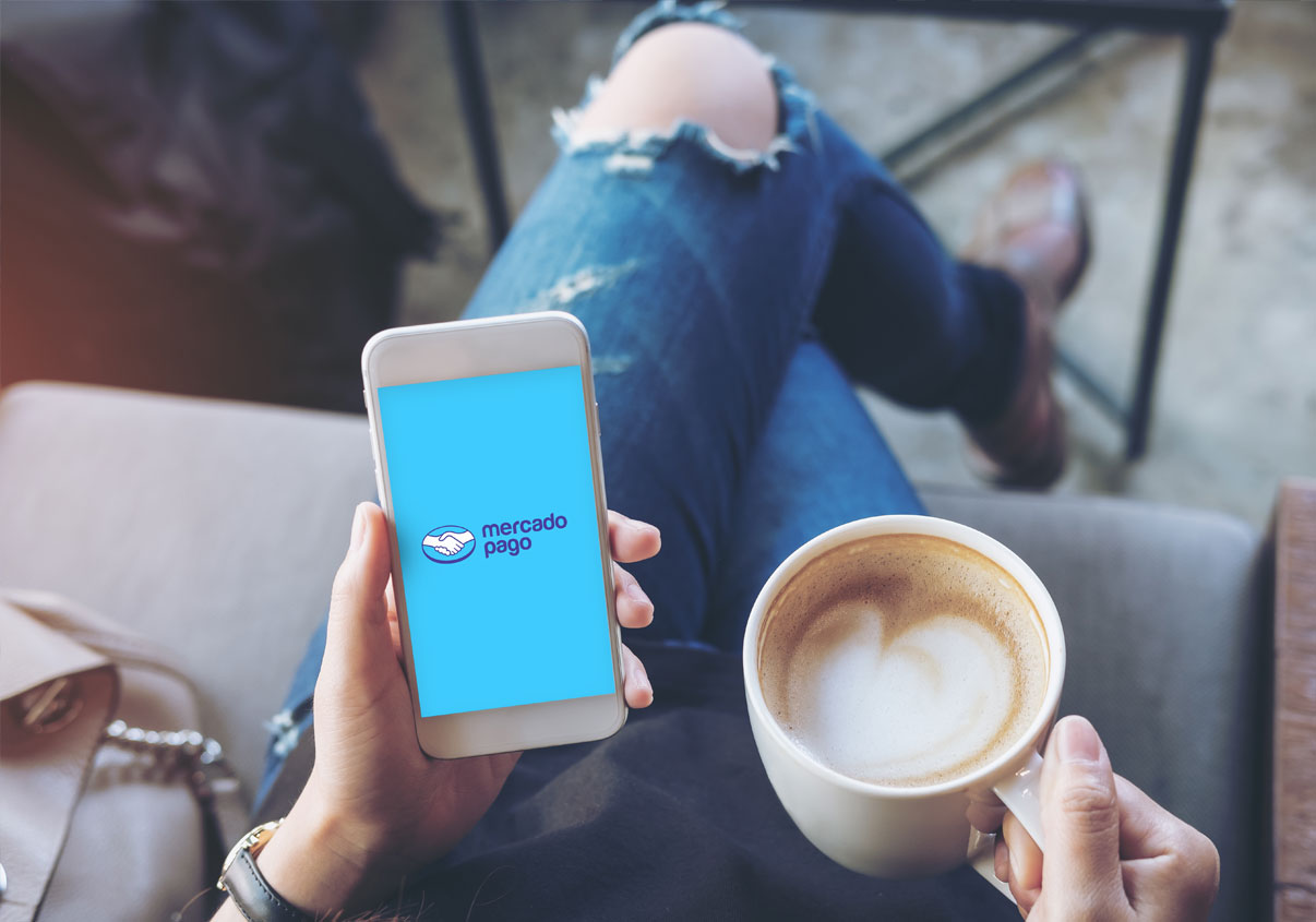 Uma pessoa segurando uma xícara de café a na outra mão segurando um celular com a tela aberta do app Mercado Pago