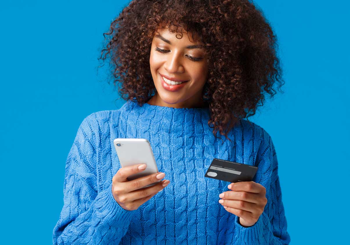 Mulher com uma blusa azul segurando o celular e um cartão em suas mãos